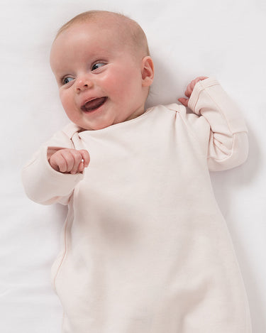 Smailing baby wearing organic cotton sleepsuit in pale pink – GOTS certified – fold over mittens and elasticated bottom – Babu