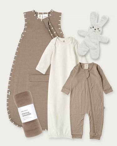 A baby sleepwear and accessory set laid out on a light beige background, including a walnut sleeveless sleep sack, a cream long-sleeve sleep gown, a walnut footless one-piece with front zipper, a rolled matching walnut blanket with a label, and a white plush bunny toy.
