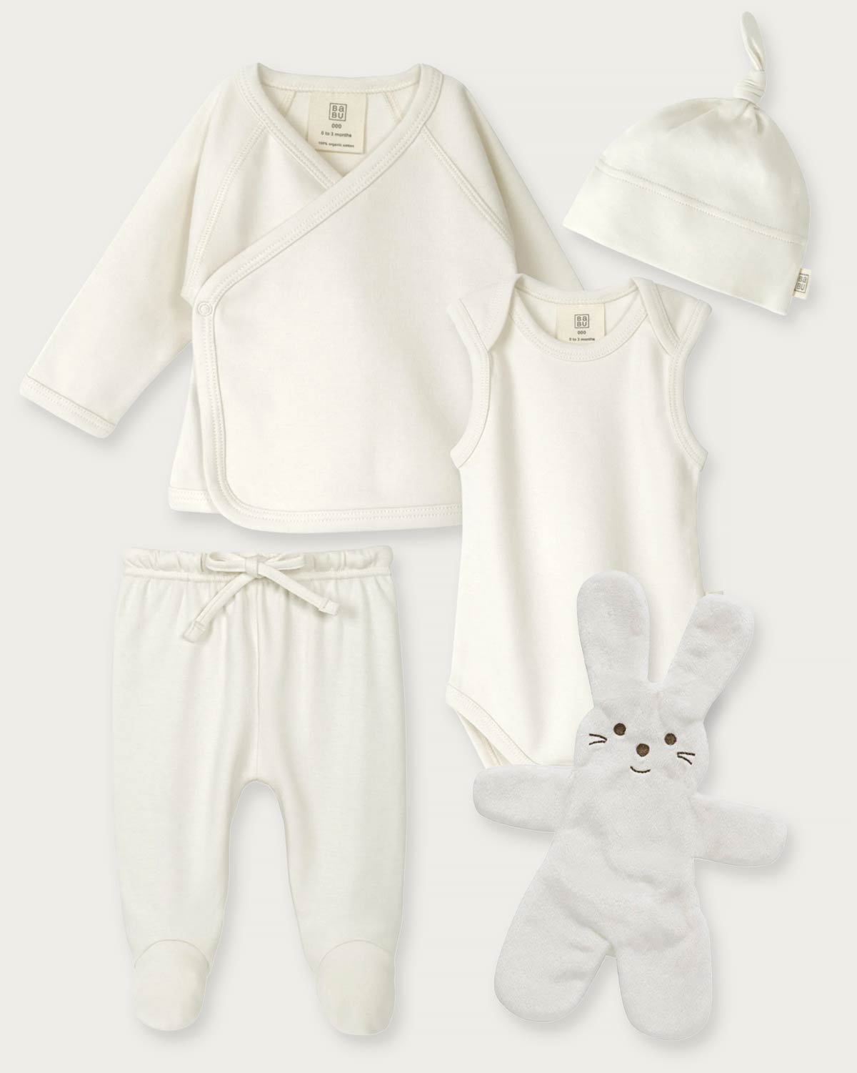 A 4-piece baby clothing set in soft off-white/cream, including a long-sleeve wrap top, sleeveless bodysuit, footed pants with a drawstring, and a knotted beanie, arranged with a plush bunny toy on a light gray background.