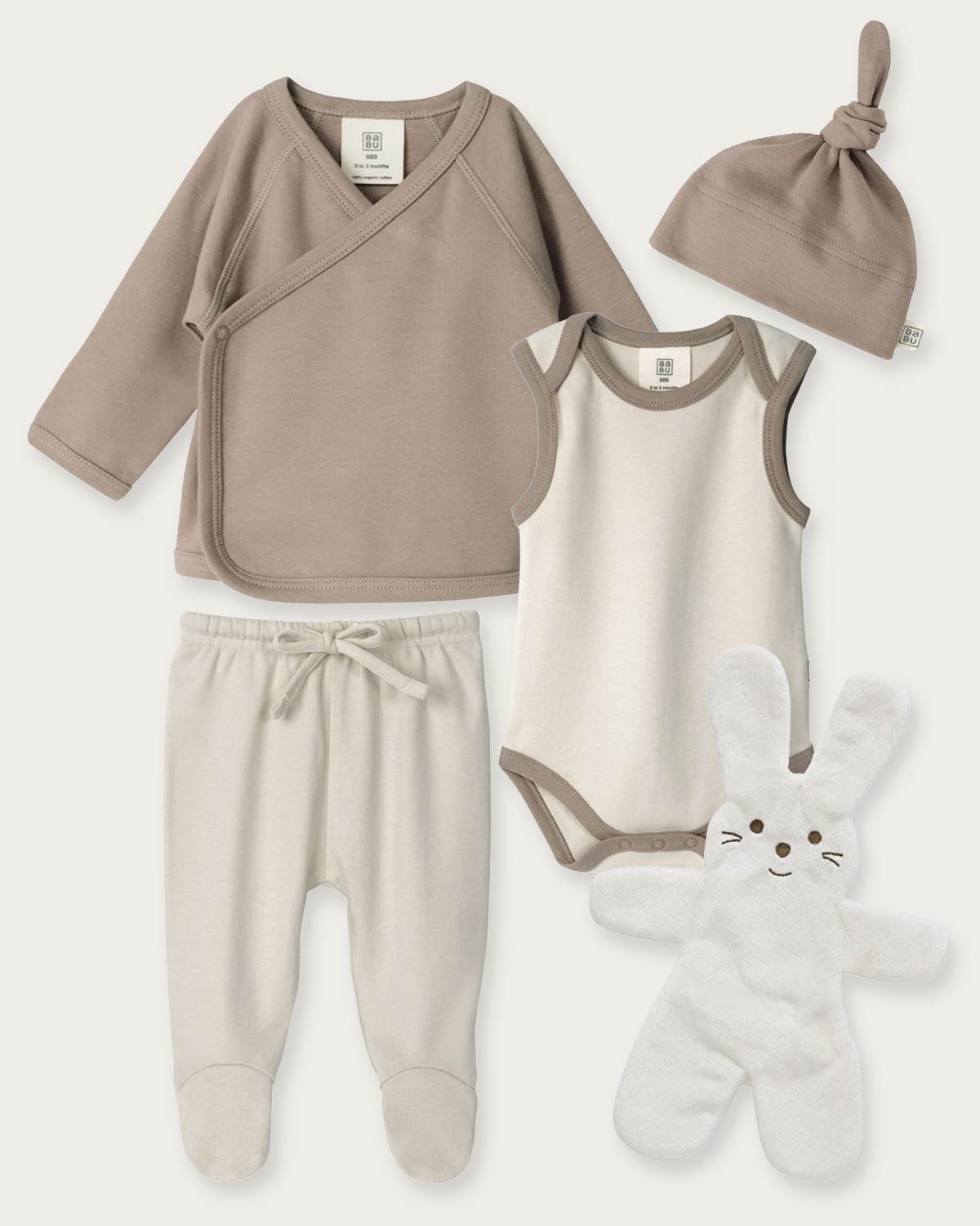 A baby clothing set laid out on a light neutral background, including a taupe wrap shirt, cream bodysuit with taupe trim, cream footed pants, a taupe knotted beanie, and a white plush bunny toy.