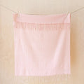 A light pink and white gingham checkered towel with fringed edges hanging from clips on a string against a light wood-paneled wall.